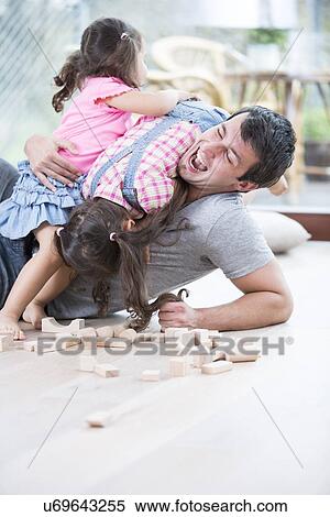 Playful daughters on top of father at home View Large Photo Image Stock Photography - Playful daughters on top of father at home. Fotosearch