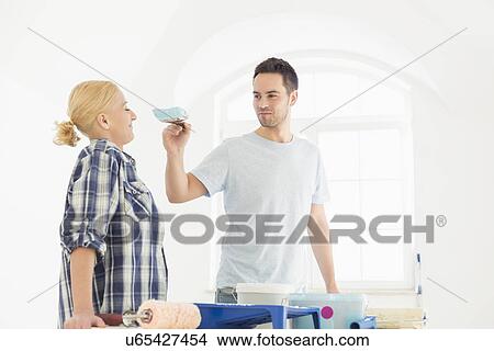 Picture - Playful man putting paint on woman's nose in new house. Fotosearch