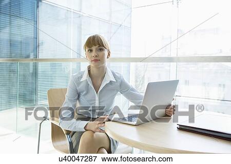 Portrait of beautiful businesswoman with laptop sitting at table in office View Large Photo Image Stock Photo - Portrait of beautiful businesswoman with laptop sitting at table in office. Fotosearch