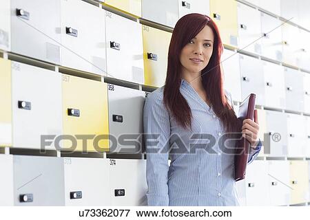 Stock Photo - Portrait of beautiful businesswoman with file standing in locker room at creative office. Fotosearch