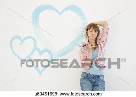Portrait of beautiful woman holding paint brush with hearts painted on wall View Large Photo Image Stock Photo - Portrait of beautiful woman holding paint brush with hearts painted on wall. Fotosearch
