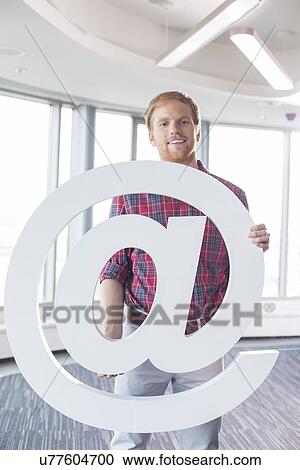 Stock Image - Portrait of confident businessman holding at sign in creative office. Fotosearch