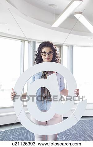 Portrait of confident businesswoman holding at symbol in creative office View Large Photo Image Stock Image - Portrait of confident businesswoman holding at symbol in creative office. Fotosearch