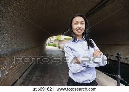 Stock Image - Portrait of confident businesswoman standing arms crossed under bridge. Fotosearch