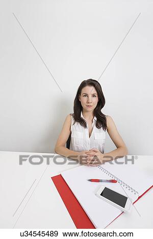 Stock Photo - Portrait of confident businesswoman with cell phone and binder at desk in office. Fotosearch
