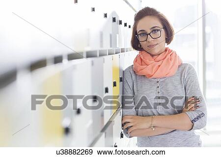 Stock Photo - Portrait of confident businesswoman standing arms crossed in locker room at creative office. Fotosearch