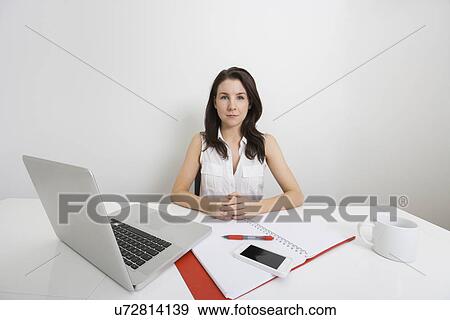 Stock Photo - Portrait of confident businesswoman with laptop and binder at desk in office. Fotosearch