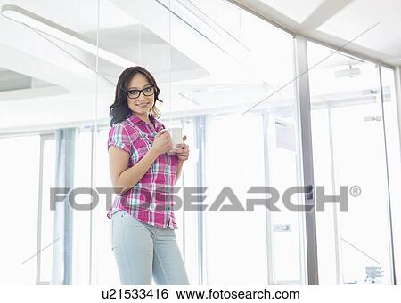 Portrait of confident businesswoman holding coffee mug in creative office View Large Photo Image Stock Photograph - Portrait of confident businesswoman holding coffee mug in creative office. Fotosearch