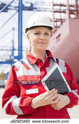 Stock Image - Portrait of confident female engineer holding tablet computer in shipping yard. Fotosearch