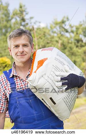 Stock Photo - Portrait of confident gardener carrying sack in plant nursery. Fotosearch