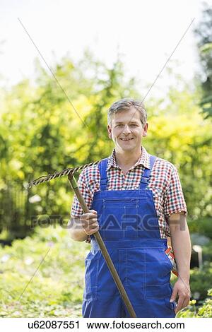 Portrait of confident gardener holding rake in plant nursery View Large Photo Image Stock Image - Portrait of confident gardener holding rake in plant nursery. Fotosearch