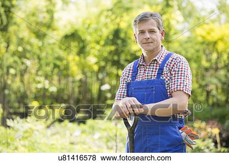 Stock Photo - Portrait of confident gardener holding spade in plant nursery. Fotosearch