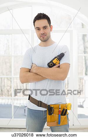 Stock Photo - Portrait of confident man with hand drill in new house. Fotosearch