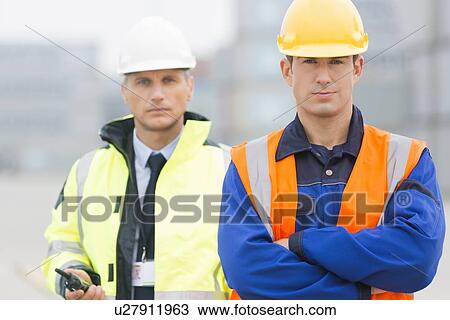 Stock Image - Portrait of confident worker standing with coworker in shipping yard. Fotosearch