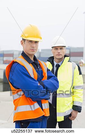 Stock Photo - Portrait of confident worker standing with coworker in shipping yard. Fotosearch