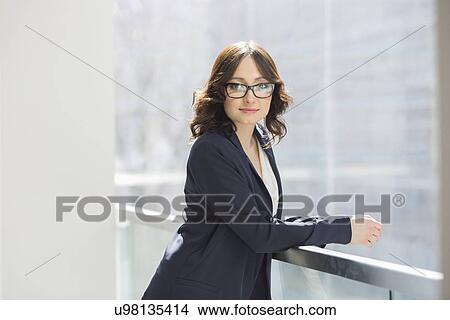 Picture - Portrait of confident young businesswoman leaning on railing in office. Fotosearch