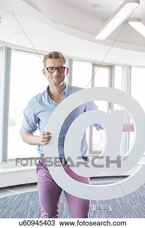 Portrait of creative businessman holding at sign in office View Large Photo Image Stock Image - Portrait of creative businessman holding at sign in office. Fotosearch
