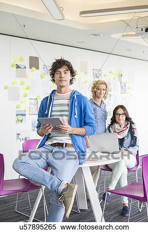 Stock Photography - Portrait of creative businessman holding digital tablet with colleagues in background. Fotosearch