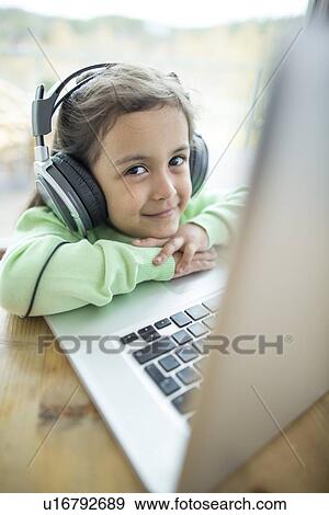Stock Photo - Portrait of cute girl listening to music on headphones while using laptop at home. Fotosearch