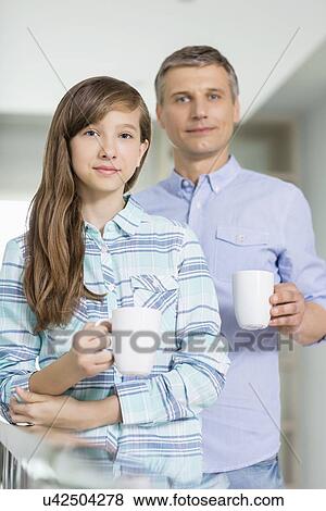 Stock Photo - Portrait of father and daughter holding coffee cups at home. Fotosearch