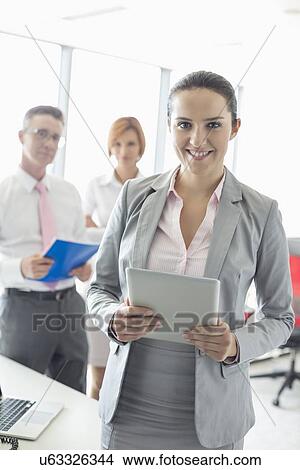 Portrait of happy businesswoman holding digital tablet with colleagues in background at office View Large Photo Image Picture - Portrait of happy businesswoman holding digital tablet with colleagues in background at office. Fotosearch