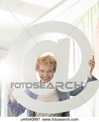 Portrait of happy businesswoman looking through at sign in creative office View Large Photo Image Stock Photo - Portrait of happy businesswoman looking through at sign in creative office. Fotosearch