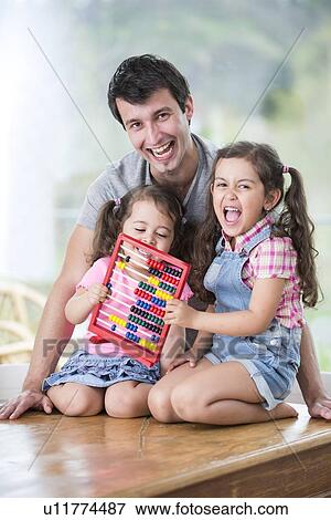 Portrait of happy father and daughters playing with abacus in house View Large Photo Image Stock Photo - Portrait of happy father and daughters playing with abacus in house. Fotosearch