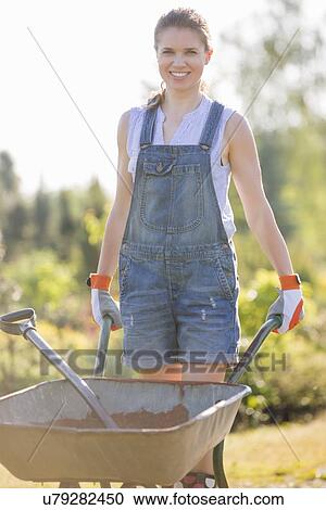 Portrait of happy female gardener pushing wheelbarrow at garden View Large Photo Image Stock Image - Portrait of happy female gardener pushing wheelbarrow at garden. Fotosearch