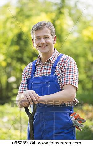 Picture - Portrait of happy gardener holding spade in plant nursery. Fotosearch