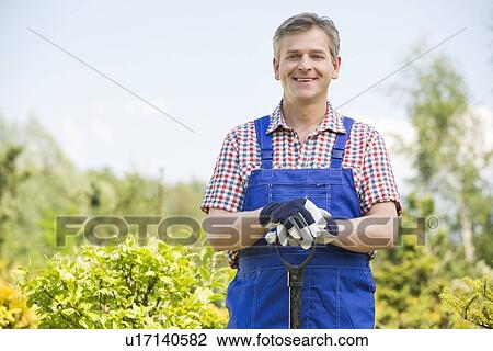 Stock Image - Portrait of happy gardener holding spade in plant nursery. Fotosearch