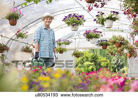 Portrait of happy man carrying watering can in greenhouse View Large Photo Image Stock Image - Portrait of happy man carrying watering can in greenhouse. Fotosearch