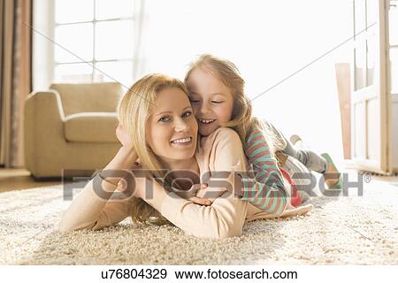 Stock Photo - Portrait of happy mother with daughter lying on floor at home. Fotosearch