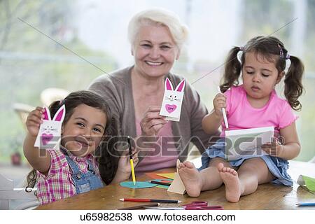 Portrait of happy senior woman showing craft rabbit while sitting with granddaughters at home View Large Photo Image Stock Photo - Portrait of happy senior woman showing craft rabbit while sitting with granddaughters at home. Fotosearch