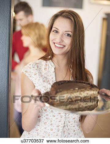 Portrait of happy woman holding cake in tray with friends in background at cafe View Large Photo Image Stock Photo - Portrait of happy woman holding cake in tray with friends in background at cafe. Fotosearch