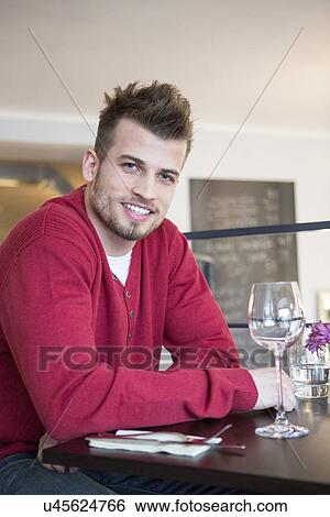 Portrait of happy young man sitting at cafe table View Large Photo Image Stock Photograph - Portrait of happy young man sitting at cafe table. Fotosearch