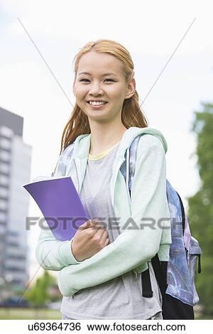 Stock Photograph - Portrait of happy young woman holding book at college campus. Fotosearch