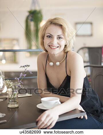 Stock Photo - Portrait of happy young woman sitting at restaurant table. Fotosearch