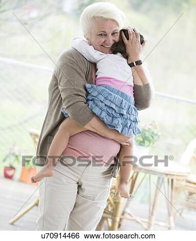 Portrait of loving grandmother carrying granddaughter at home View Large Photo Image Stock Photograph - Portrait of loving grandmother carrying granddaughter at home. Fotosearch