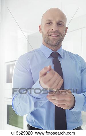 Stock Image - Portrait of mid adult businessman buttoning sleeve at home. Fotosearch