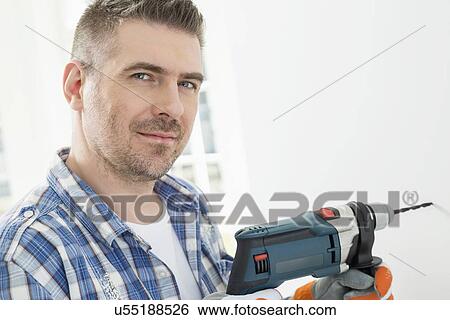 Stock Photograph - Portrait of mid-adult man drilling hole in wall. Fotosearch