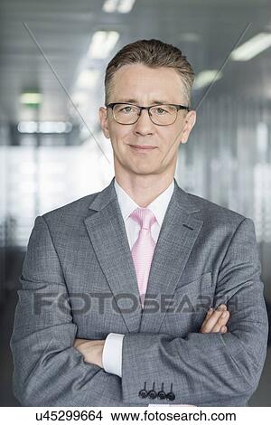 Portrait of middle-aged businessman standing with arms crossed in office View Large Photo Image Picture - Portrait of middle-aged businessman standing with arms crossed in office. Fotosearch