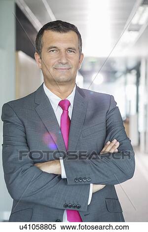 Stock Photography - Portrait of middle-aged businessman standing with arms crossed in office. Fotosearch