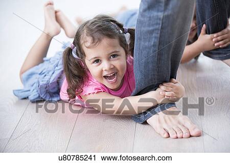 Portrait of playful girl with sister holding father's legs on hardwood floor View Large Photo Image Stock Image - Portrait of playful girl with sister holding father's legs on hardwood floor. Fotosearch