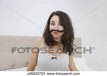 Stock Image - Portrait of playful woman with mustache made of hair in bed. Fotosearch