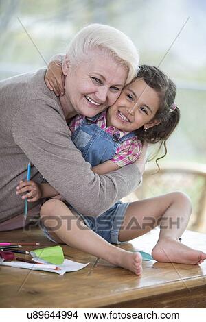 Portrait of senior woman hugging granddaughter sitting on table at home View Large Photo Image Picture - Portrait of senior woman hugging granddaughter sitting on table at home. Fotosearch
