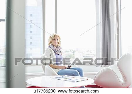 Stock Image - Portrait of smiling businesswoman sitting at creative office lobby. Fotosearch