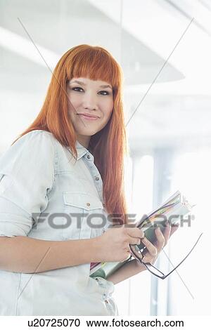 Portrait of smiling businesswoman holding files in creative office View Large Photo Image Stock Image - Portrait of smiling businesswoman holding files in creative office. Fotosearch