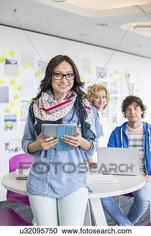 Portrait of smiling businesswoman holding digital tablet with colleagues in background at creative office View Large Photo Image Stock Image - Portrait of smiling businesswoman holding digital tablet with colleagues in background at creative office. Fotosearch