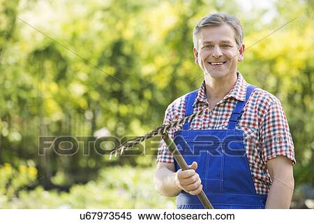 Stock Photography - Portrait of smiling gardener holding rake in plant nursery. Fotosearch