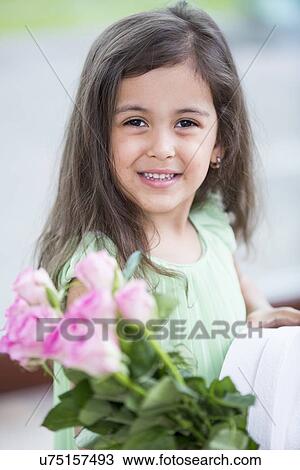 Stock Image - Portrait of smiling girl holding roses and gift box at home. Fotosearch